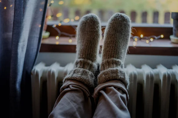 Women\'s legs feet in woolen socks on a heating radiator. Heating in winter concept, women\'s legs feet in woolen socks on a heating battery
