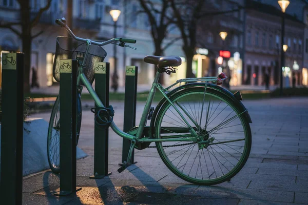 Green city bike on bicycle parking in evening city, modern background