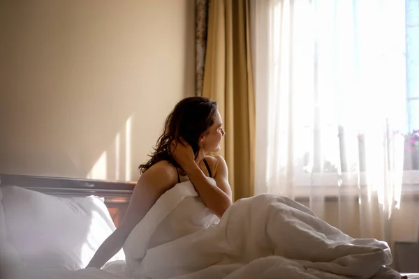 Beautiful young happy relaxed woman in the morning sitting in bed looking out the window