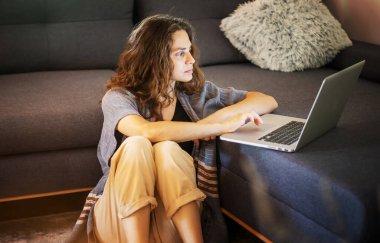 Young woman using laptop at home sitting on floor near sofa, work and education online