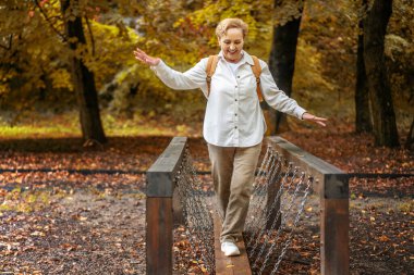 Beautiful happy caucasian active senior woman enjoying nature in autumn park. Active pensioners lifestyle concept