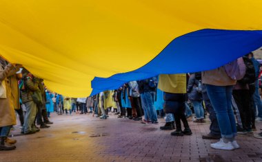 A crowd of people holding a large national Ukrainian flag at a rally in support of Ukraine against Russia's war