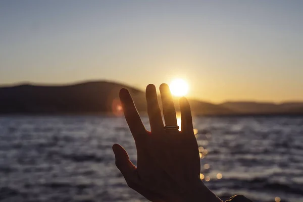 海岸の日没時に女性の手のひらの指の間の太陽 — ストック写真