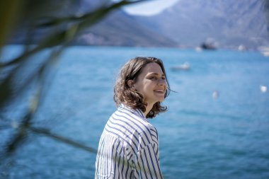 Genç, mutlu, gülümseyen kadın güneşin altında kıyıda oturuyor. Yaz tatili