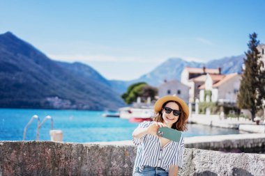 Şapkalı genç bir kadın, Akdeniz 'de bir tatil köyünde akıllı telefon kullanarak selfie çekiyor.