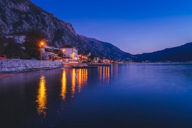 Güzel gece manzarası. Gece ışıklarındaki Kotor Körfezi seti ve su yüzeyindeki parlak binaların yansıması.