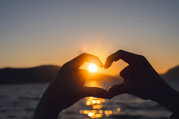 日落时 海滨的女人的手指在形成心形 热爱旅行的概念 — 图库照片