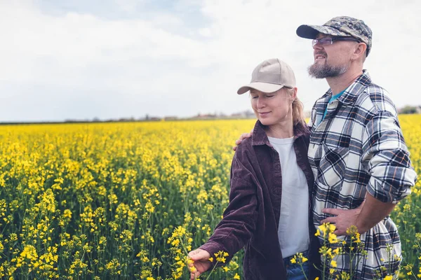 Young adult caucasian couple of farmers standing in a spring blooming rapeseed field