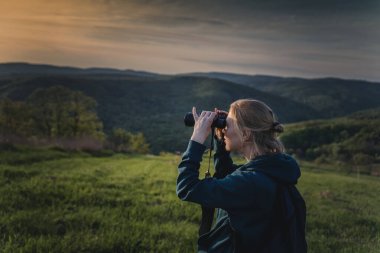 Dişi yürüyüşçü yeşil ormanda kuş gözlemi için dürbün kullanıyor.