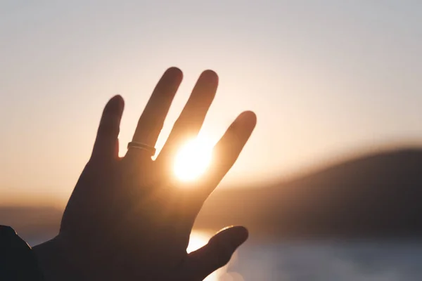 海岸の日没時に女性の手のひらの指の間の太陽 — ストック写真