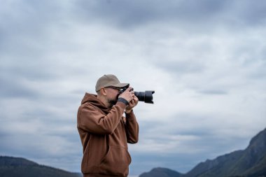 Genç yetişkin erkek gezgin, puslu dağ manzaralı kamera kullanarak fotoğraf çekiyor.