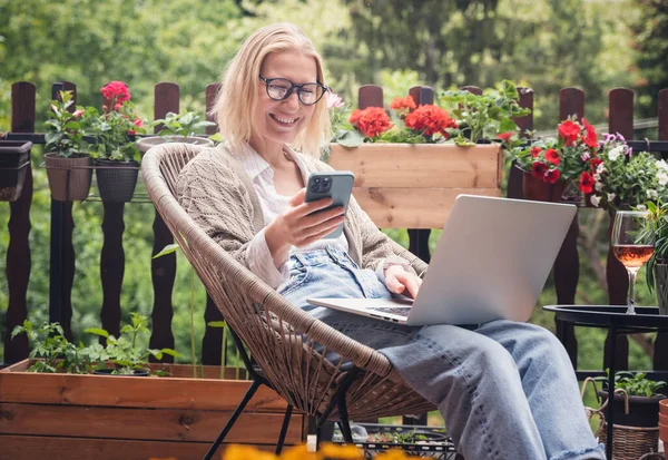 美しい金髪の中年女性は夏にカントリーハウスのテラスでリラックスし オンライン作業のためのラップトップを使用しています — ストック写真