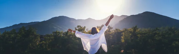 一位身穿白衬衫 双手高举的妇女 在黎明时分 在高山的背景下享受晨阳 — 图库照片