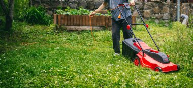 Elektrikli çim biçme makinesi kullanan bir kadın. Yaz bahçesi bakım konsepti