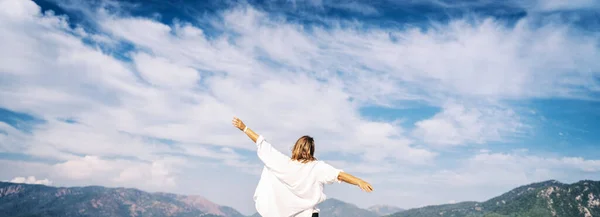 一个穿着白衬衫的女人在风中飘扬 在天空和高山的衬托下 — 图库照片