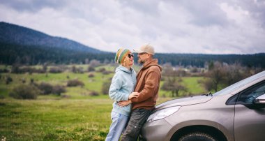 Romantik mutlu orta yaşlı çift dağlarda otomobil yolculuğu sırasında arabaların yanında birbirlerine sarılıyorlar.