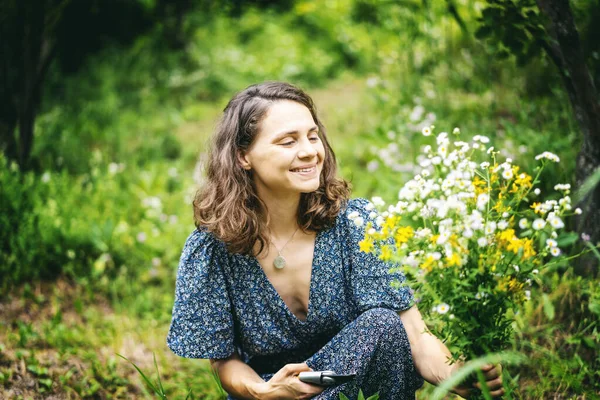 Młoda Uśmiechnięta Kobieta Letniej Sukience Zbierająca Bukiet Dzikich Kwiatów Ogrodzie — Zdjęcie stockowe