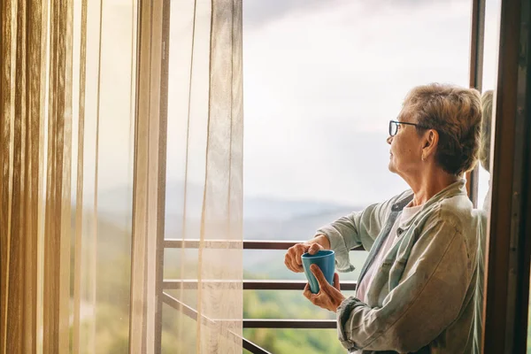 Güzel Yaşlı Bir Kadın Pencerenin Önünde Durmuş Dağlara Bakıyor Elinde — Stok fotoğraf