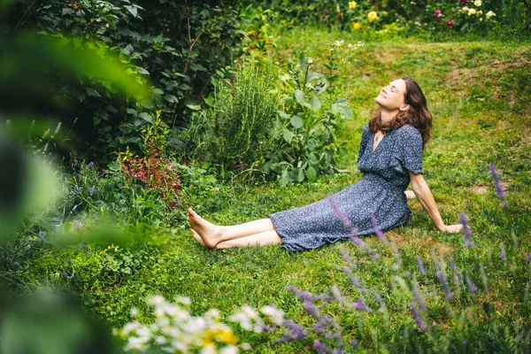庭の緑の草の上に座っている間 夏をリラックスして楽しむドレスの幸せな若い女性 — ストック写真