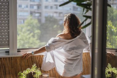Beyaz gömlekli beyaz bir kadın sabah balkonda dikiliyor ve yeni bir günle tanışıyor.