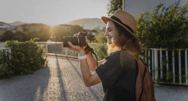 Bir yaz şehrinde elinde fotoğraf makinesi olan şapkalı beyaz bir kadın gezgin.
