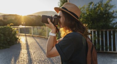 Bir yaz şehrinde elinde fotoğraf makinesi olan şapkalı beyaz bir kadın gezgin.