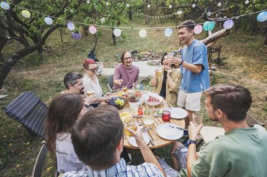 Bir grup mutlu genç yetişkin bahçede barbekü partisinde eğleniyor. Kutlama, yaz tatili ve arkadaşlık.