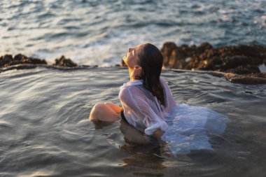 Deniz kıyısında doğal bir deniz banyosunda beyaz gömlekli, neşeli, rahat bir kadın. Thalasapi sağlıklılığı