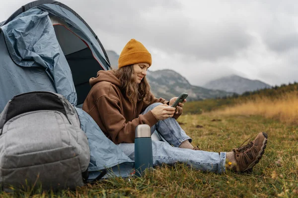 Young cheerful woman traveling with a tent using a smartphone. Hiking and trekking lifestyle