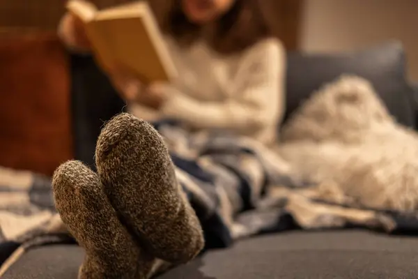 Women\'s feet in warm woolen socks. Cozy winter evening at home, woman sitting on the sofa with a book