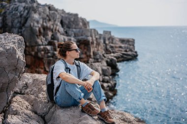 Gezgin kadın. Kayalık deniz kıyısında dinleniyor. Manzaranın tadını çıkarıyor.