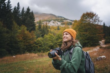 Gezgin kadın fotoğrafçı, dağlara ve ormana sonbahar gezisi sırasında kamera kullanarak fotoğraf çekiyor.