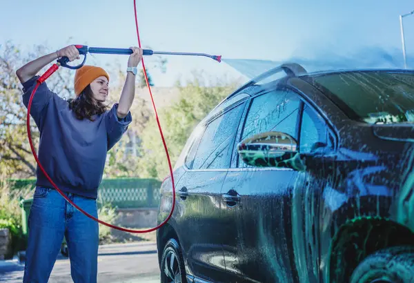 Woman cleaning auto with high pressure water jet at a self-service car wash