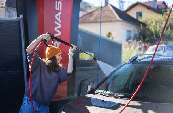 Woman cleaning auto with high pressure water jet at a self-service car wash