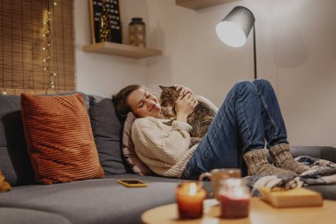 Evde tekir kediyle rahat, kanepede evdeki evcil hayvanıyla kadın, kış tatili konsepti.