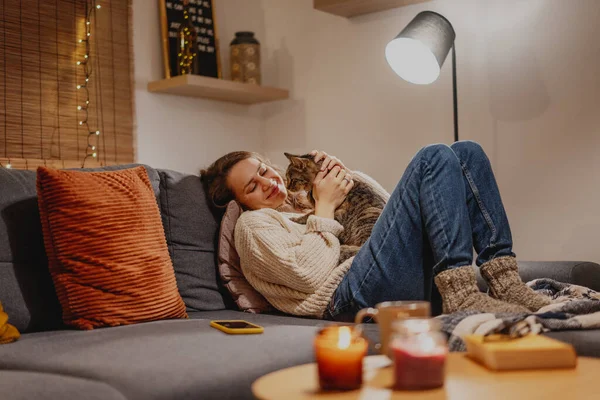 Cozy at home with tabby cat, woman with her pet on sofa ay home in evening, Winter holidays concept