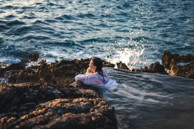 Deniz kıyısında doğal bir deniz banyosunda beyaz gömlekli, neşeli, rahat bir kadın. Thalasapi sağlıklılığı