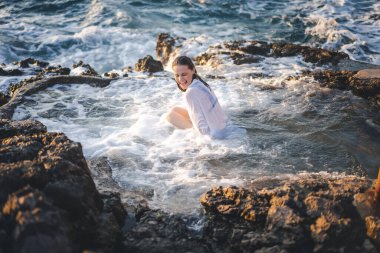 Deniz kıyısında doğal bir deniz banyosunda beyaz gömlekli, neşeli, rahat bir kadın. Thalasapi sağlıklılığı