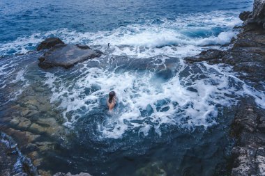 Bulutlu havada deniz dalgaları olan bir göldeki kadın, doğal deniz banyosu konsepti.