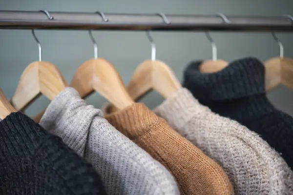 Warm wool sweaters in neutral colors hanging on hangers. Warm winter clothes concept