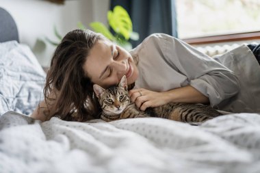 Gri kedisi olan genç bir kadın sabahları yatakta uyanıyor.