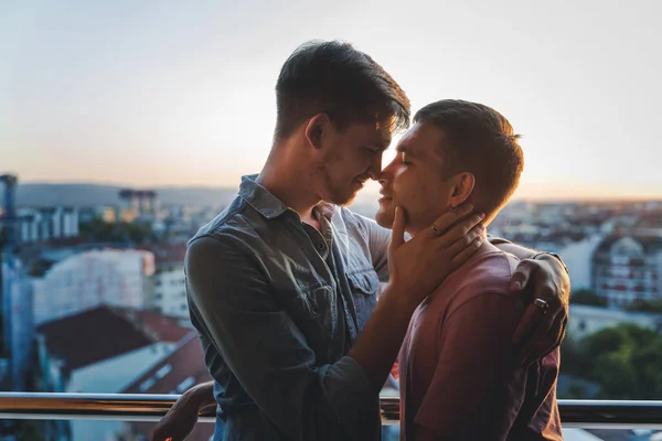 若い幸せなかわいいゲイ カップル 抱擁し 街を見下ろすバルコニーでキス ロイヤリティフリーのストック写真