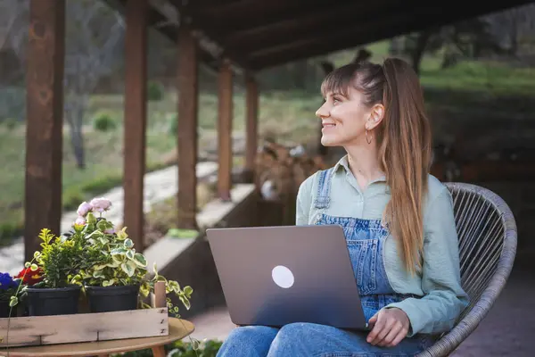 Jonge Gelukkig Vrouw Denim Overalls Zitten Met Een Laptop Het Rechtenvrije Stockafbeeldingen