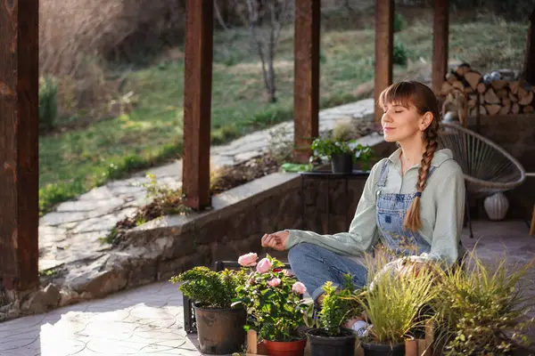 若い幸せな女性は春の日に花の鍋の中でテラスに蓮の位置に座って瞑想しています ロイヤリティフリーのストック写真