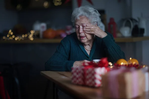 Unhappy senior woman sitting alone and crying during Christmas Eve. Concept of solitude seniors.