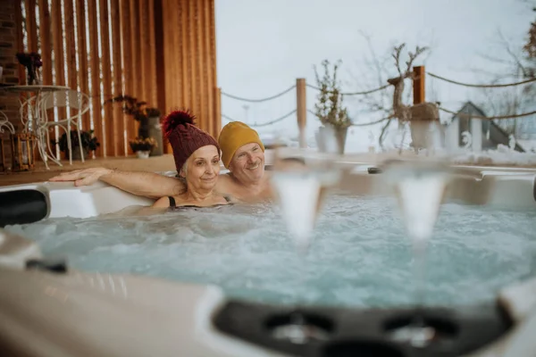 在寒冷的冬日里 头戴针织帽子的老夫妇在阳台上一起享受户外浴缸 — 图库照片