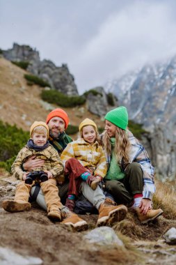 Sonbahar dağlarında yürüyüş yaparken mutlu bir aile oturup dinleniyor..