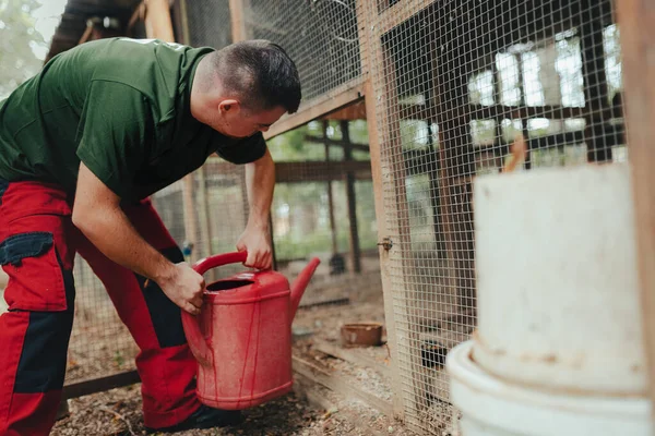 動物園のダウン症の介護者は動物の囲いの中で水を与えます 障害者を社会に統合するという概念 — ストック写真