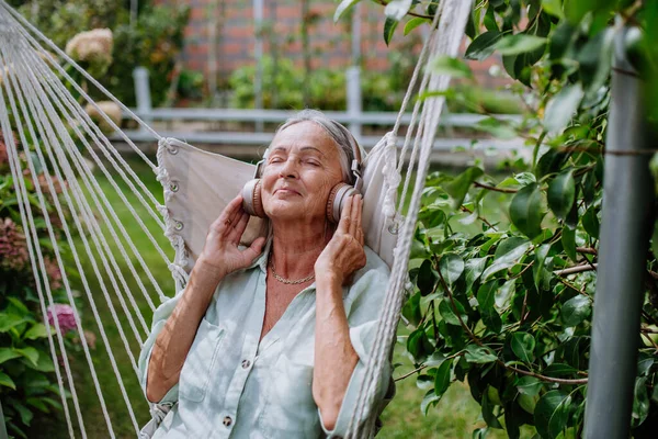 庭のスイングでリラックスしたシニア女性 音楽を聞いてスルーヘッドフォン — ストック写真