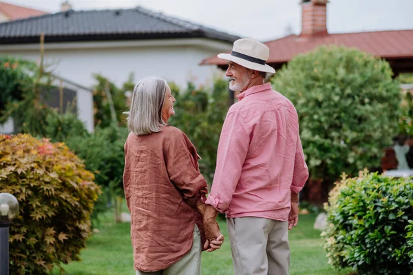 庭で一緒にポーズを取り 互いの手を保持する高齢者のカップルの背面ビュー — ストック写真